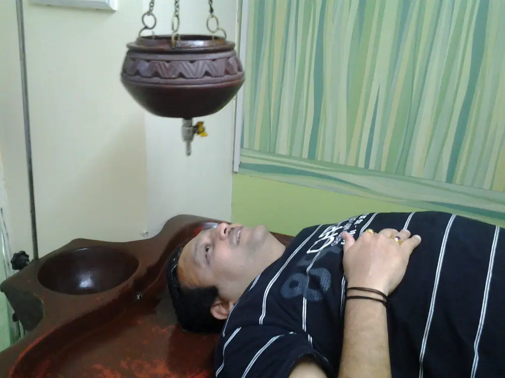 A shirodhara pot above a treatment table, mid-session